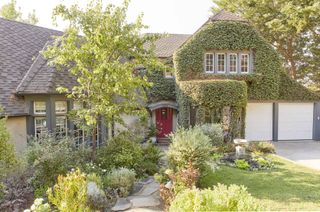 An example of front yard landscaping ideas showing a house with a mélange of leafy greens, a stone walkway, water fountain and tomato red front door