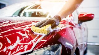Someone cleaning a soapy car with a sponge