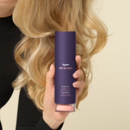 Blonde curly hair with hand holding up dyson chitosan pre-styling cream 