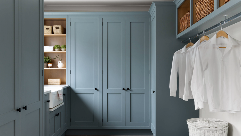 Utility room with blue cabinets and shirts hanging on a rail underneath baskets