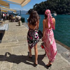 two woman wearing printed dresses walk by the waterfront