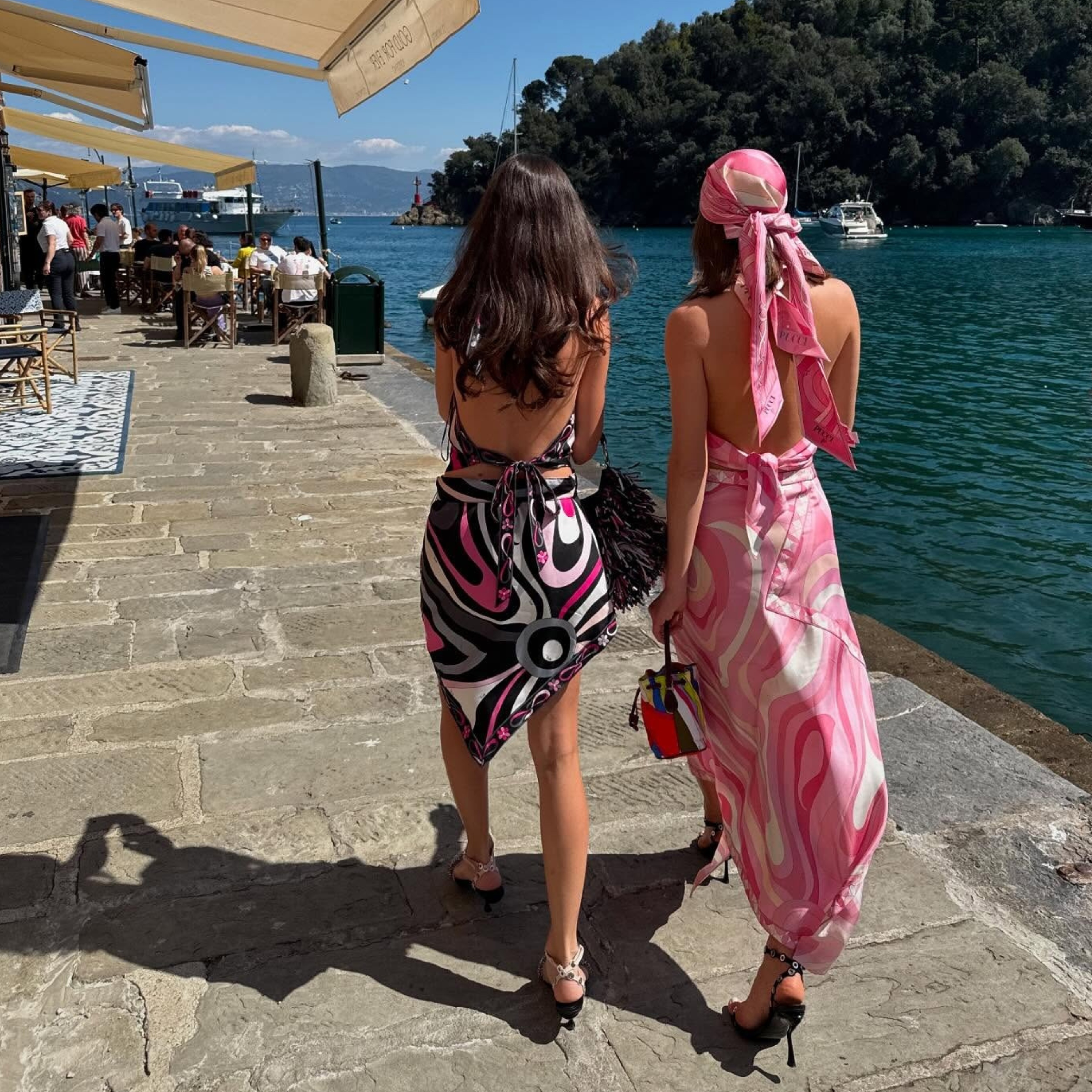 two woman wearing printed dresses walk by the waterfront