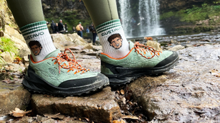 a picture of the keen jasper zionic hiking shoes in green/gold colorway being worn on a hiking trail with a waterfall in the background