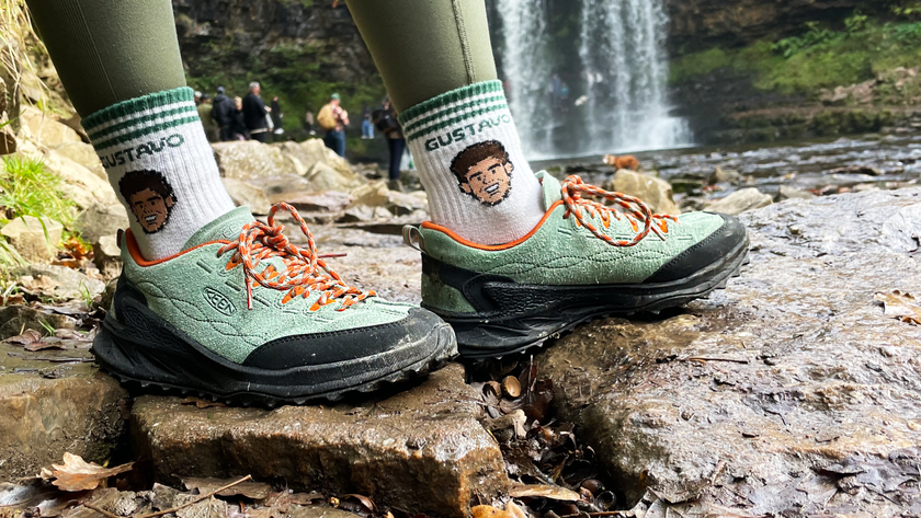 a picture of the keen jasper zionic hiking shoes in green/gold colorway being worn on a hiking trail with a waterfall in the background