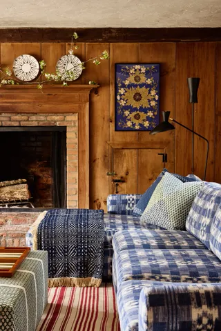 In a country living room, multiple blankets, throws and rugs with geometrical motifs placed on sofas sited in front of a fireplace recreate an intimate environment.