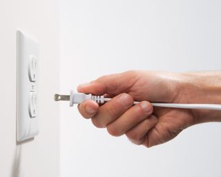 Close up of a person's hand holding a plug about to plug into outlet on the left