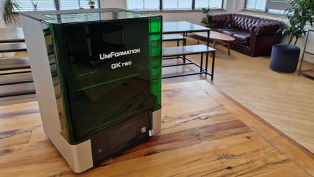 The Uniformation GKtwo on a wooden table, with a sofa and plants in the background