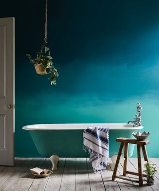 blue bathroom with ombre painted wall, painted tub, wooden floor boards, stool