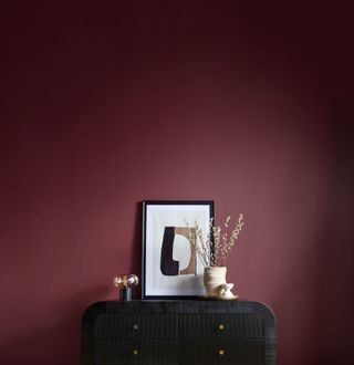 A room with a black sideboard and burgundy painted walls