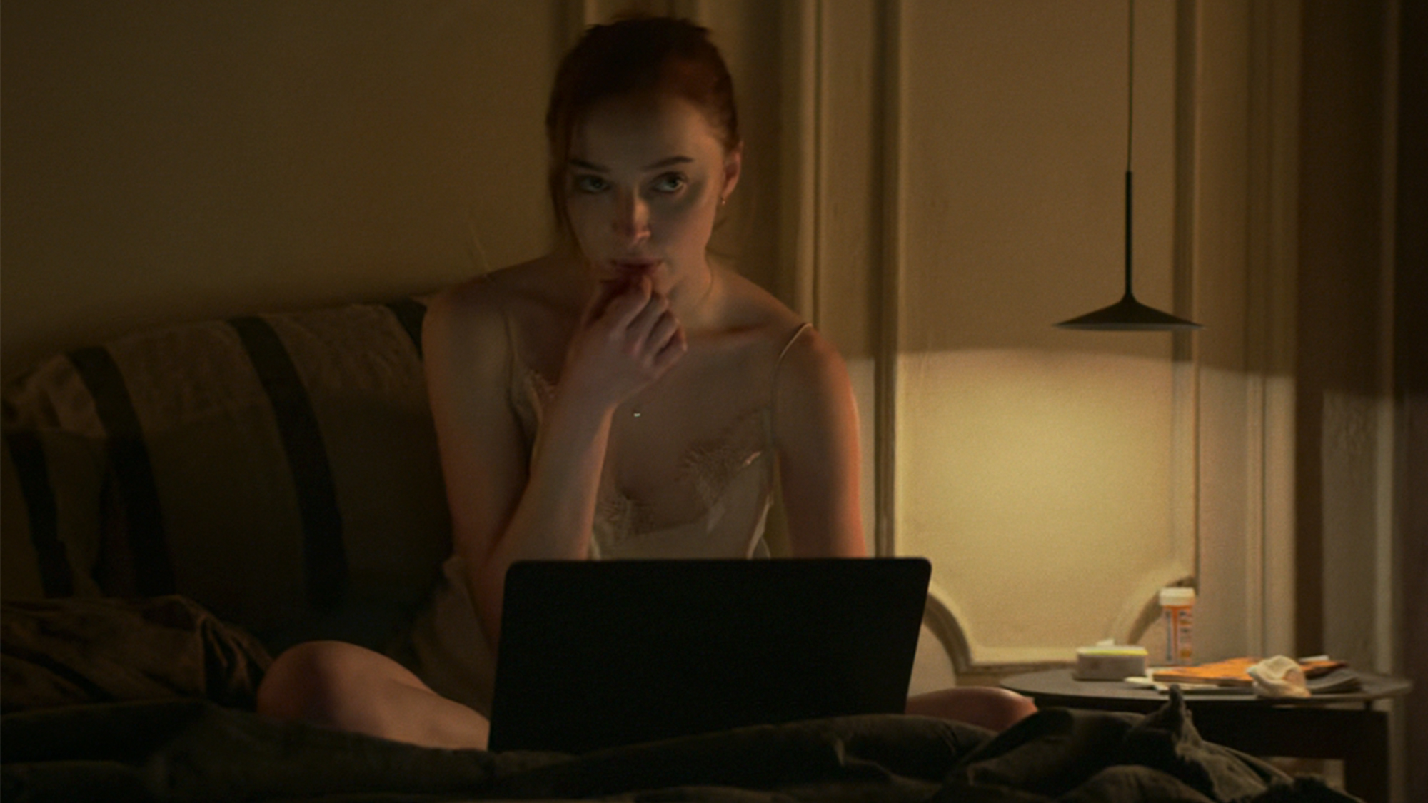 A woman sitting on a bed, looking at a laptop