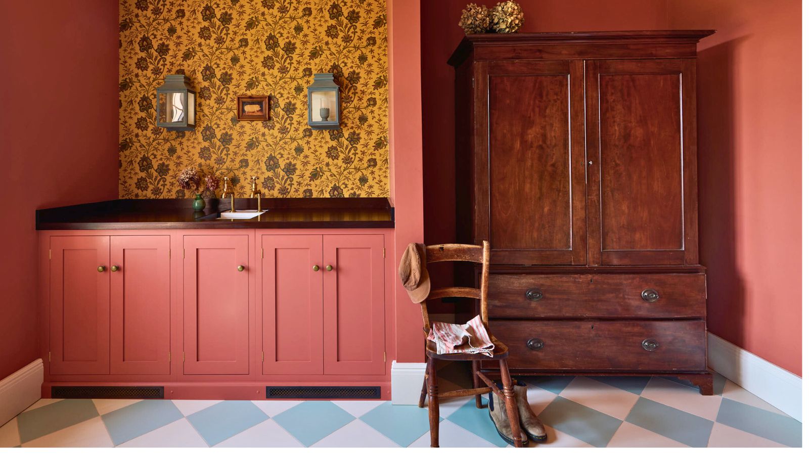 Dark orange kitchen utility area with dark yellow wallpaper. The floor is blue and white diamond pattern and there is a combination of built-in lower cabinets, and freestanding mid-century cabinet