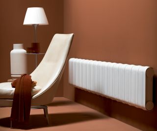 white radiator in room with cream chair, table with white lamp and terracotta coloured walls