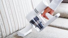 Vacuuming white sofa with handheld vacuum