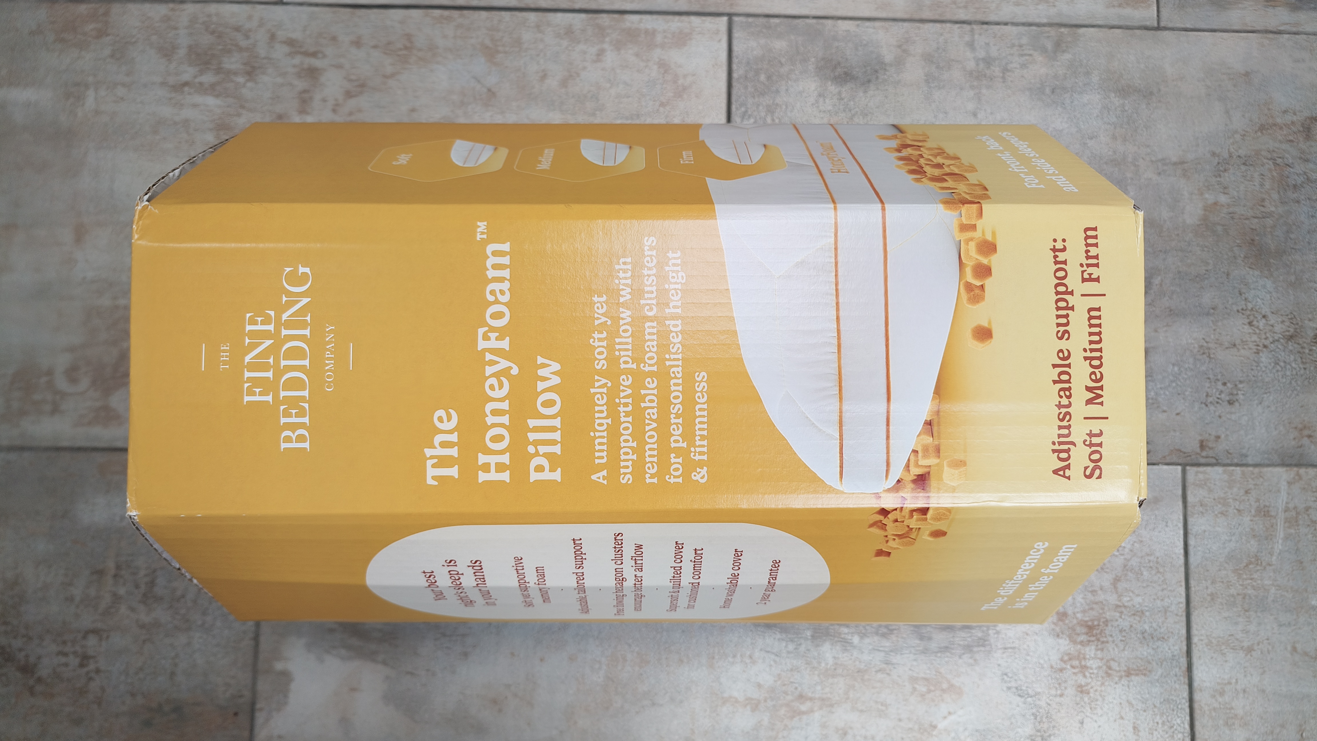 The yellow product packaging for "The HoneyFoam Pillow" by The Fine Bedding Company, highlighting features like adjustable support and removable foam clusters.