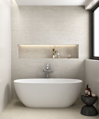A small white bathtub with textured wall backgrop and lit cubby