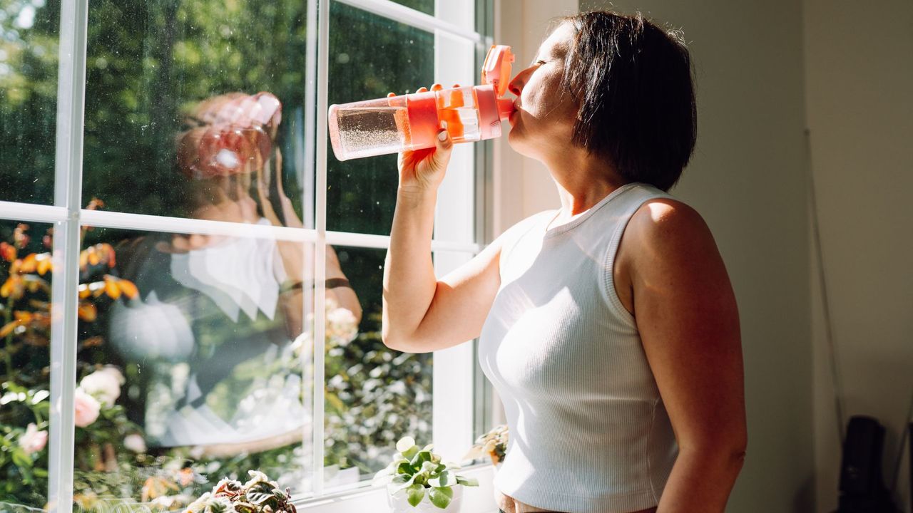 Woman drinking water looking out of window wearing activewear 