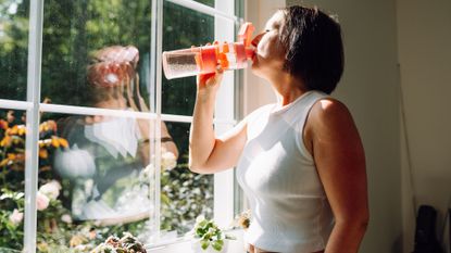 Woman drinking water looking out of window wearing activewear 