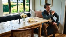 Nate Berkus poses alongside his Rugs USA collaboration inside of a sunlit breakfast nook with a wooden table