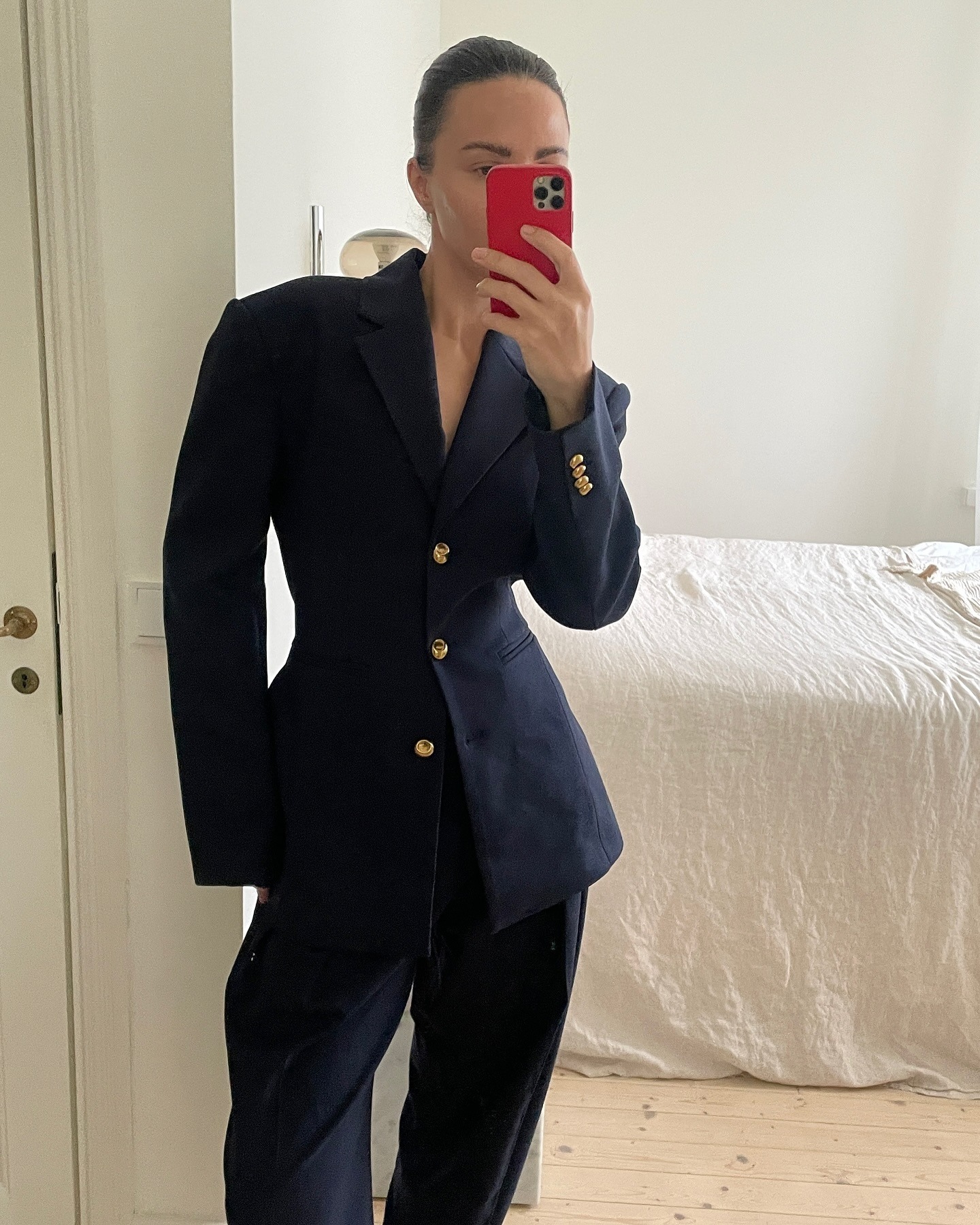 Style influencer Johanna Piispa poses for a mirror selfie wearing a waisted navy blazer suit jacket with yellow-gold buttons and matching navy pants.