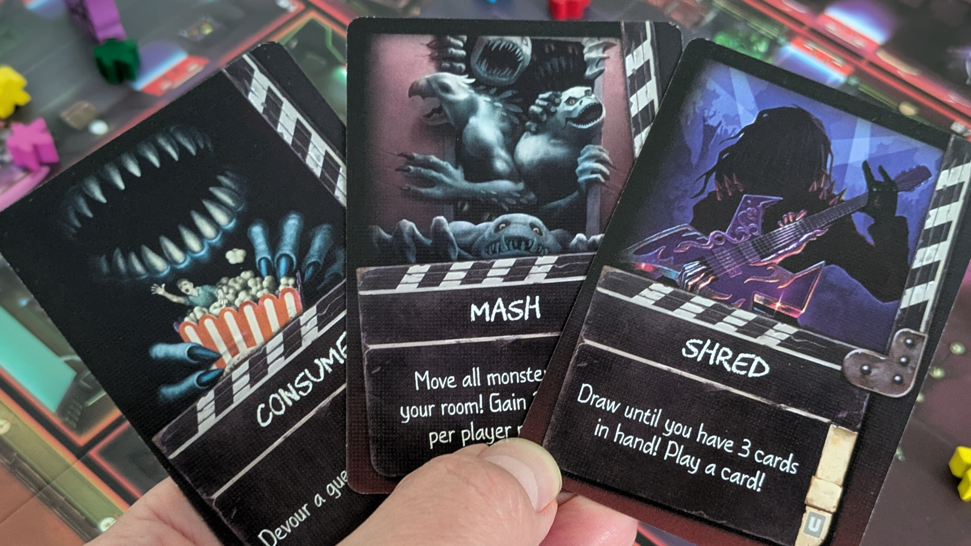A hand holds up three Spooktacular cards in front of the board