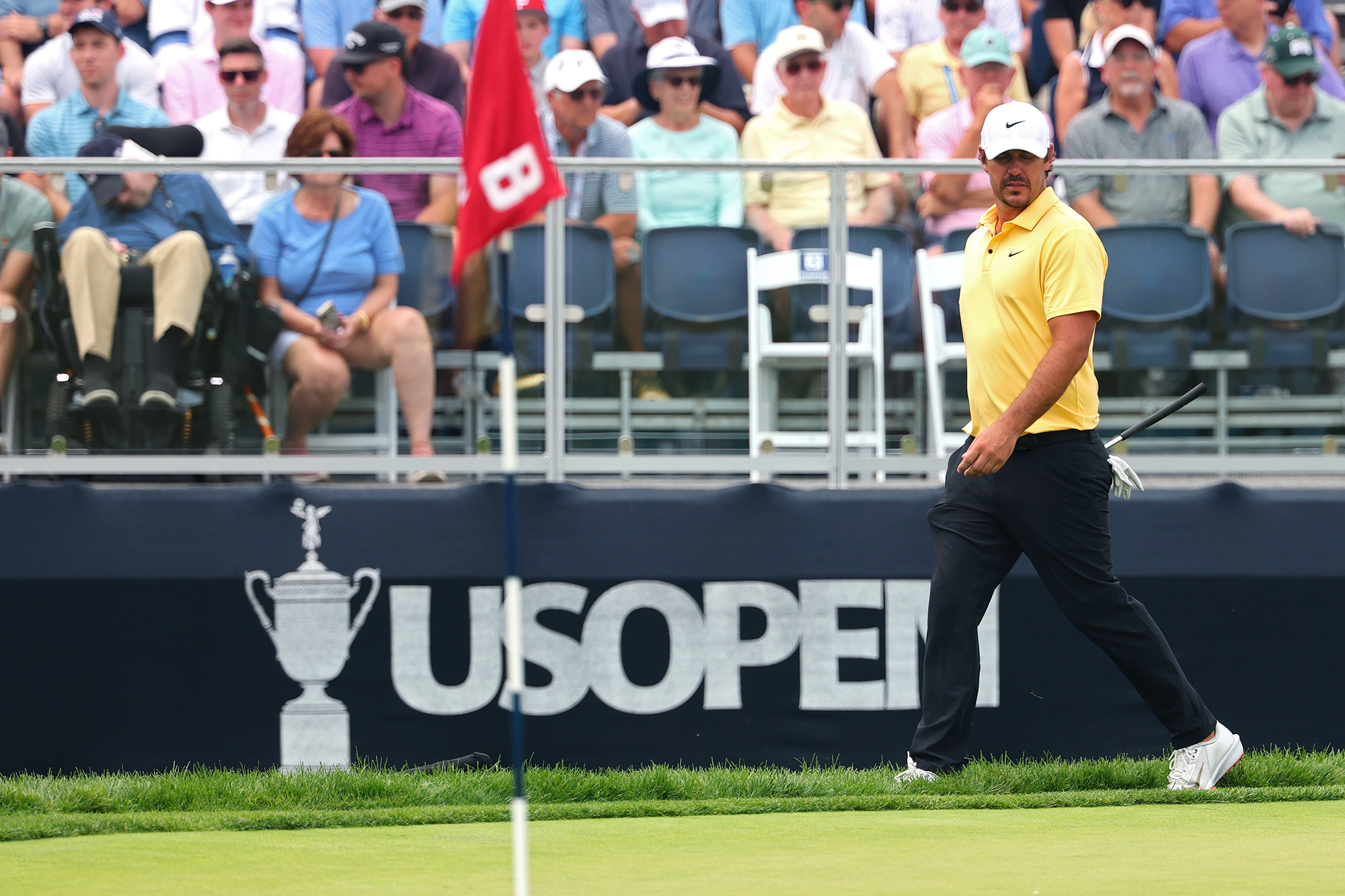 Brooks Koepka walking around the green and in front of the grandstand at the 8th hole of the 2025 US Open
