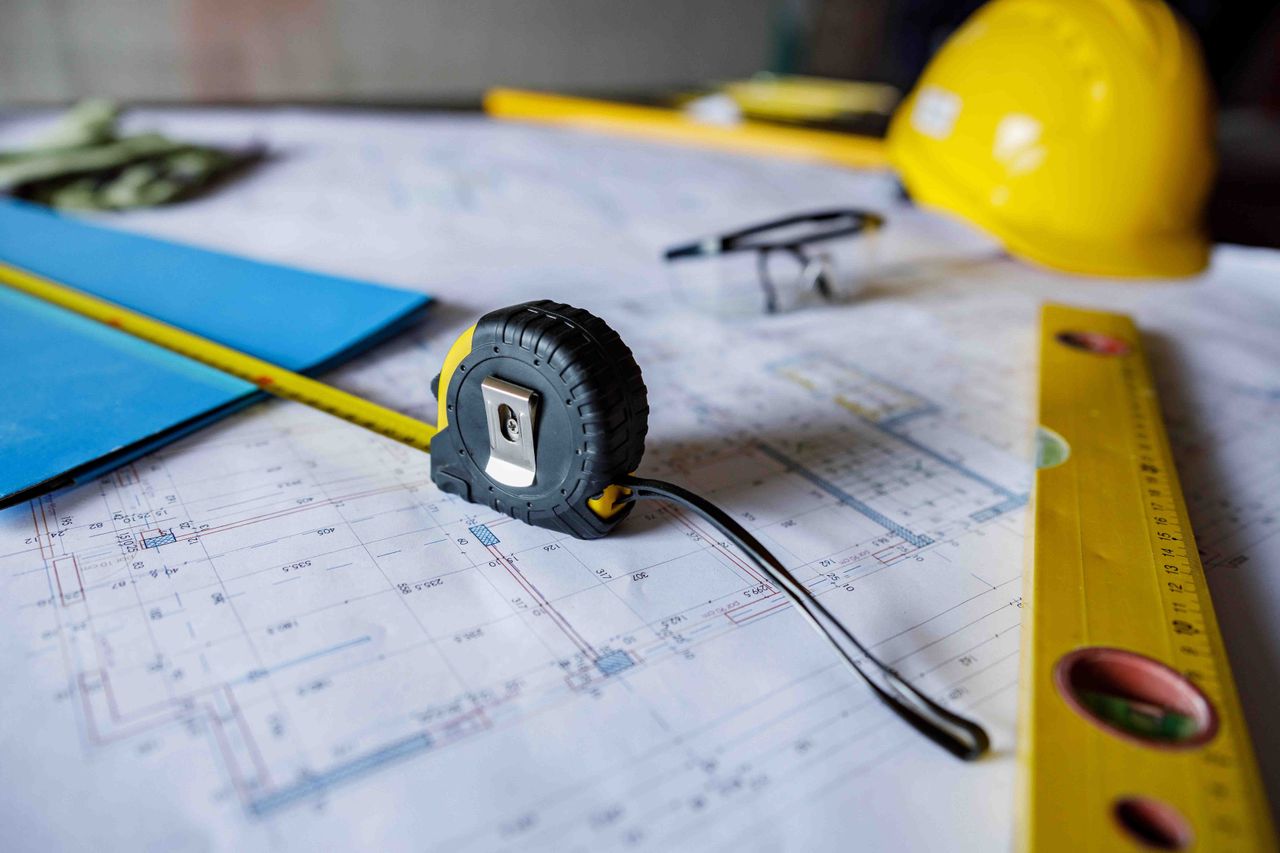 items, including a tape measure, a level, a hard hat and a folder sit atop architectural drawings