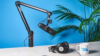 a black microphone by cherry XTRFY with a branded muff and an XLR and USB-C port sits atop a pale brown desk with a dark blue background