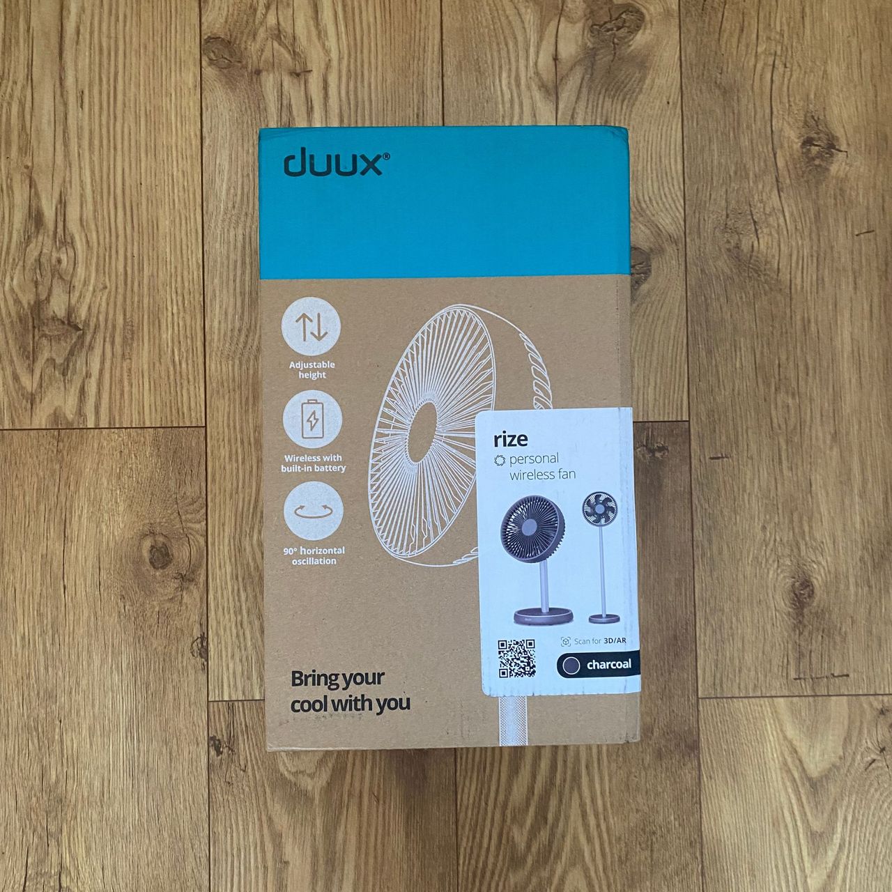 The cardboard packaging of the Duux Rize fan on a wood-look LVT floor