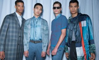 Four models wearing Brioni fashion, one with checked grey suit, three wearing casual grey and turquoise clothing