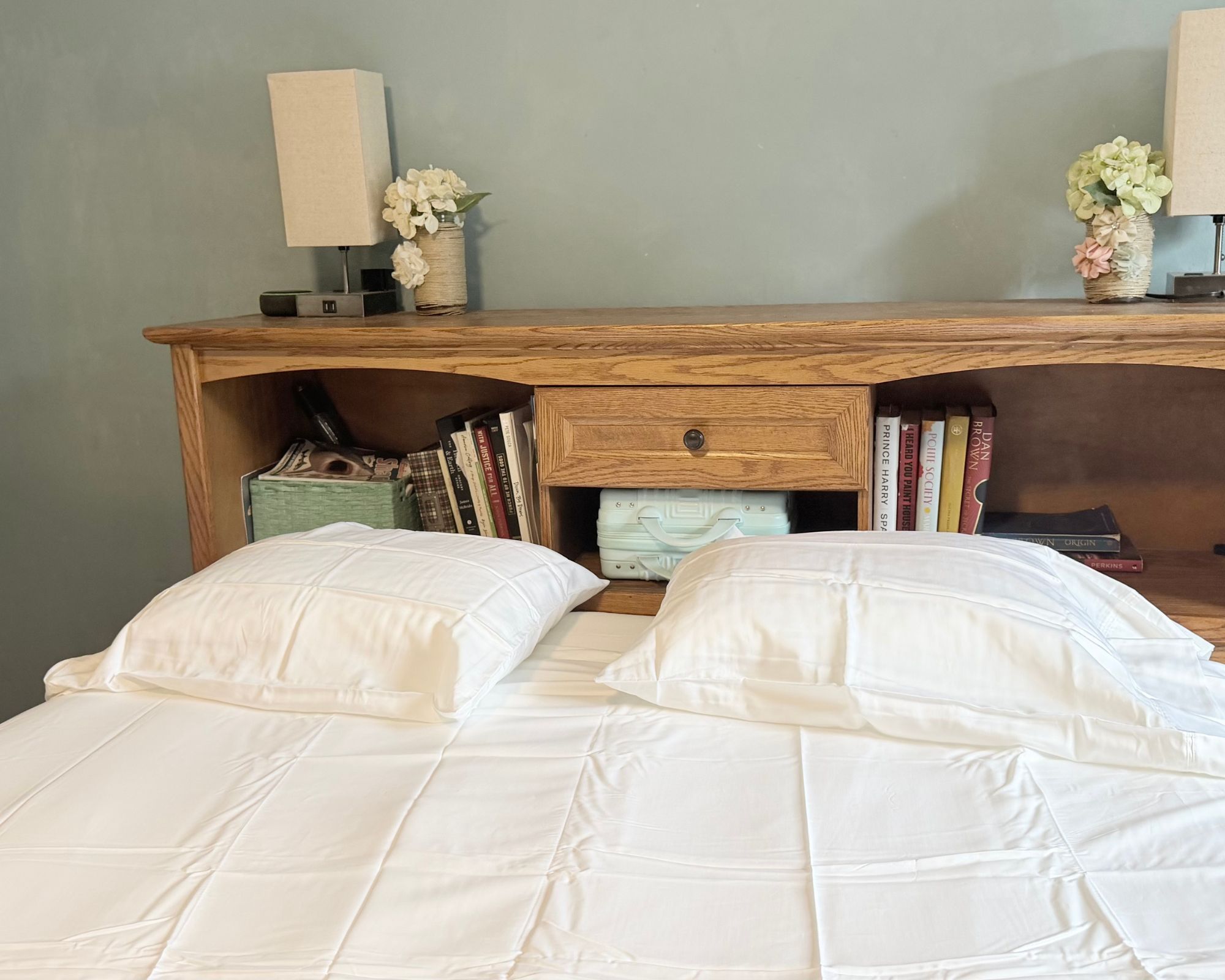 Sleep Number ComfortNext bed with white bedding and a wooden headboard filled with books behind, with two matching lamps and vases of flowers on top.