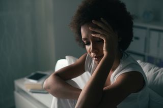 A woman sitting on a bed looking tired.