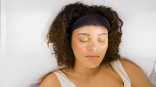 A woman lies in bed wearing the Elemind neurotech headband, she's sleeping peacefully