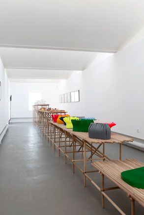 Colourful art display on long wooden tables in a room with white walls and grey floor