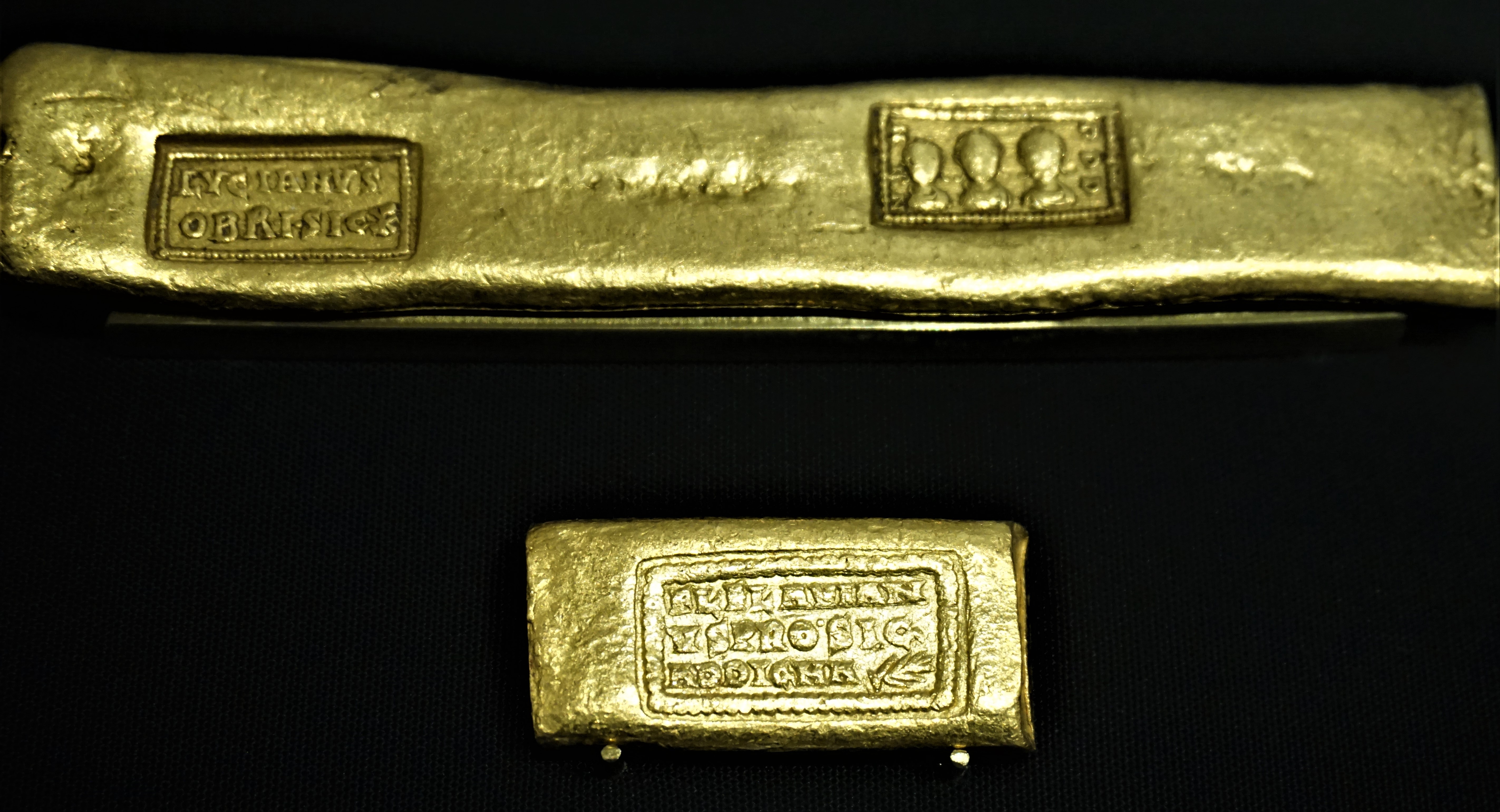 A close up and a regular picture of two rectangular gold ingots on a black background.