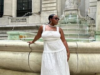 Aniyah wears white dress and white fisherman sandals while posing in front of a large fountain.