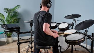 Drummer wearing headphones shot from behind an electronic drum set