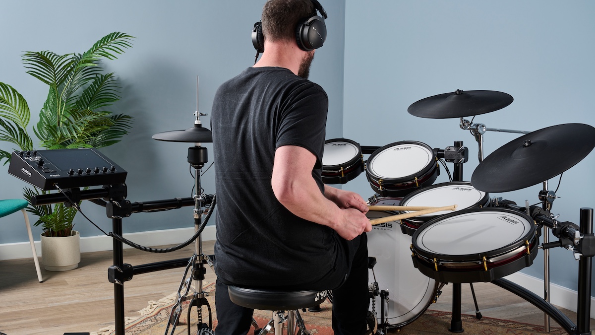 Drummer wearing headphones shot from behind an electronic drum set