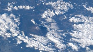 the snow-capped peak of a mountain is seen from far above the clouds in a photo taken by an astronaut on a space station.