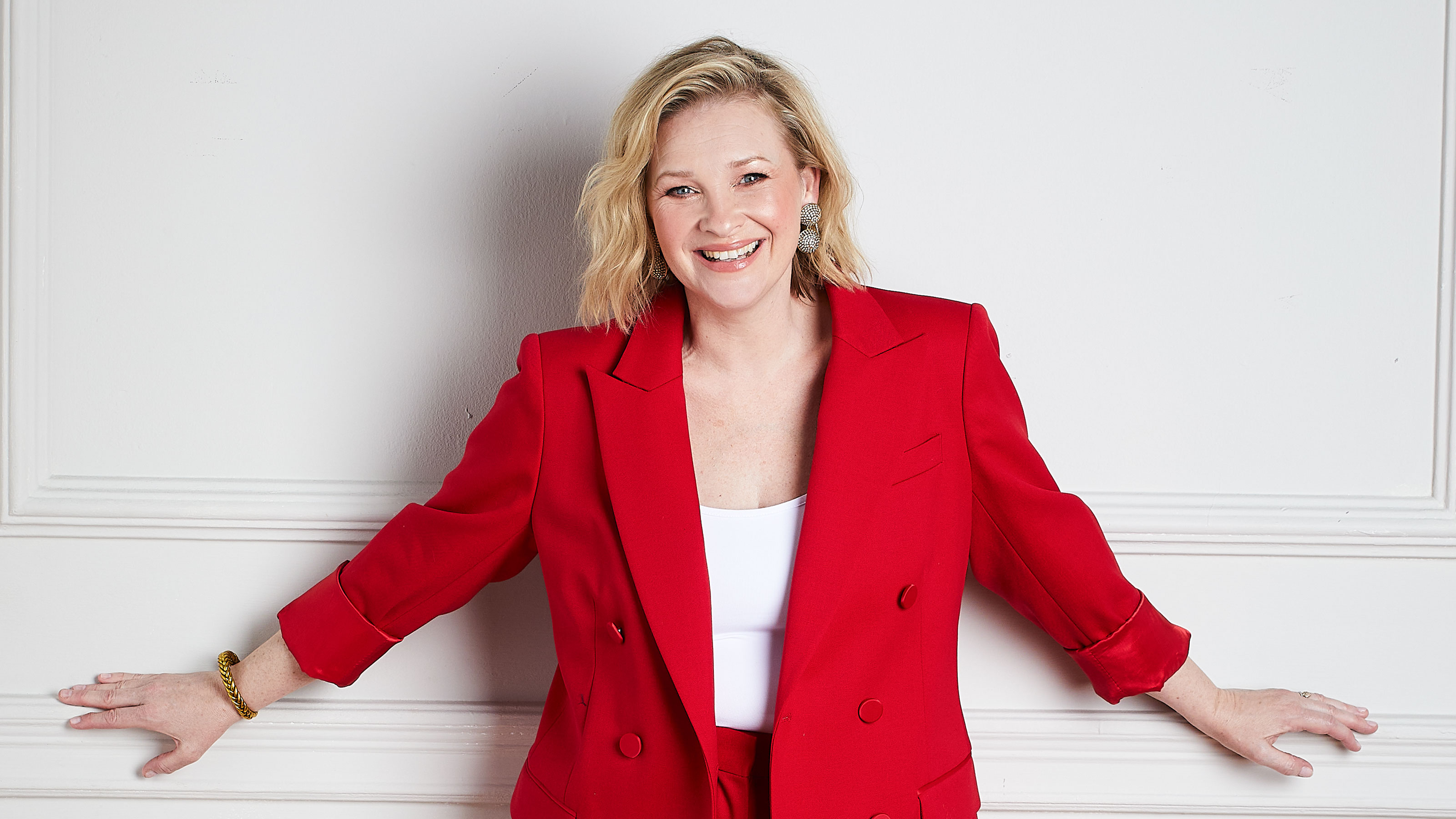 Joanna Page in a red outfit posing against a plain grey background