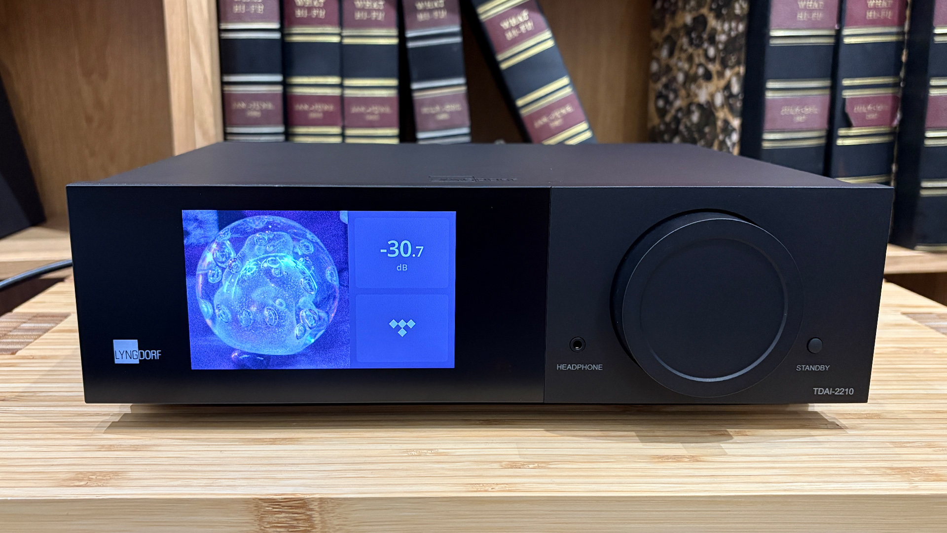 Lyngdorf TDAI-2210 streaming amplifier on wooden hi-fi rack in front of bookcase