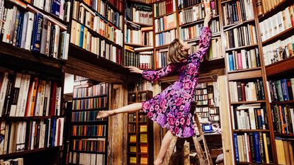 Carefree woman on ladder reaching for book in library