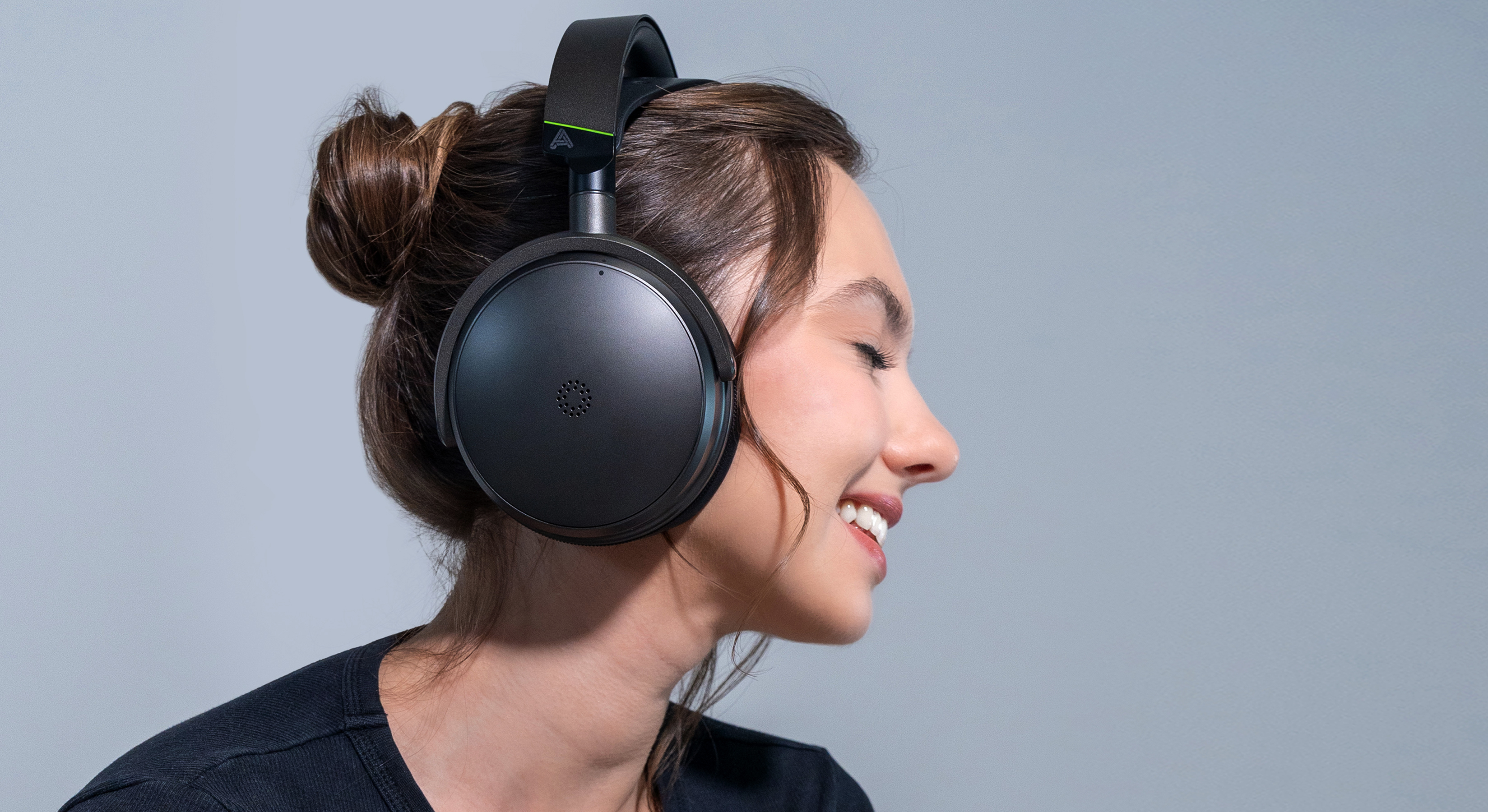 A young woman in a black top wearing the Audeze Maxwell 2 gaming headset against a grey/blue background