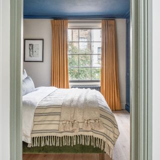 accent colour ideas, bedroom with blue painted ceiling and wardrobe, turmeric curtains, green bed with off white and oatmeal bedding, artwork, wooden floor