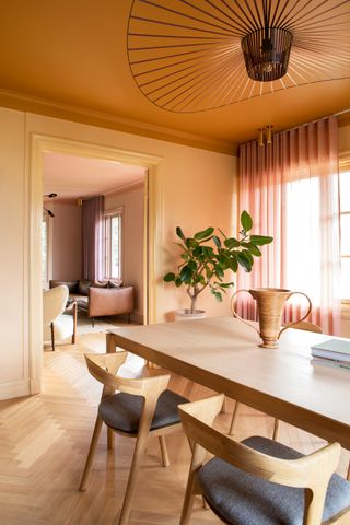 a dining room and living room in orang and pink terracotta shades with a parquet floor and dramatic pendant light