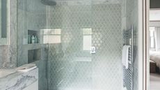 A marble and glass tiled shower with a shower niche, large glass screen, silver radiator and marble sink