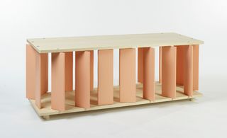 A wooden object with multiple peach pillars photographed against a grey background