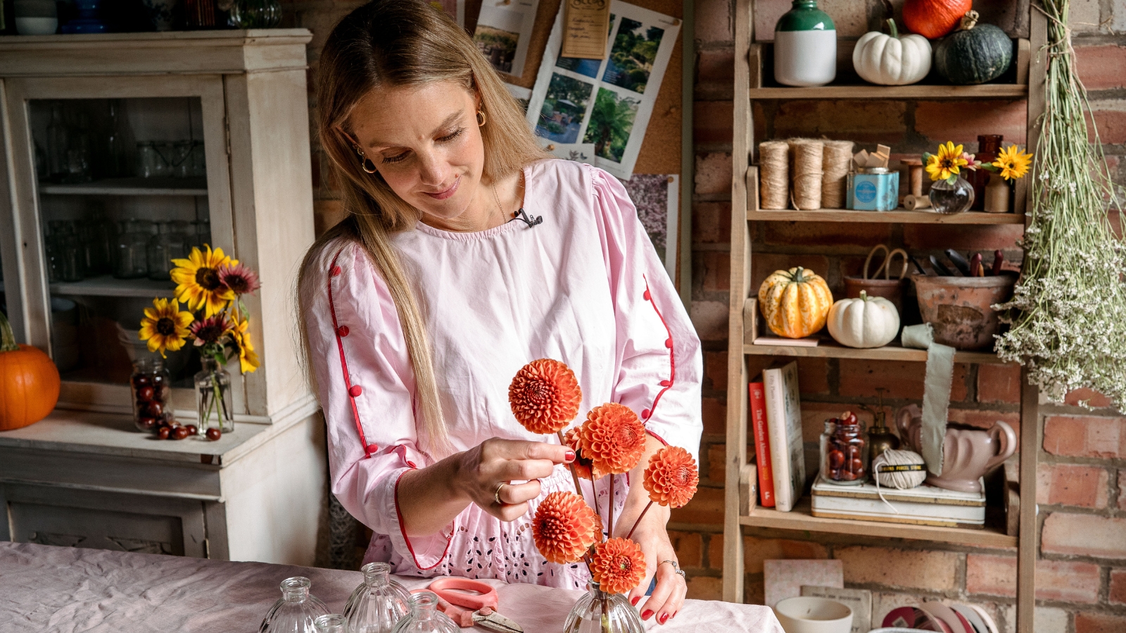 Woman placing orange dahlias into bud vase in floristry workshop