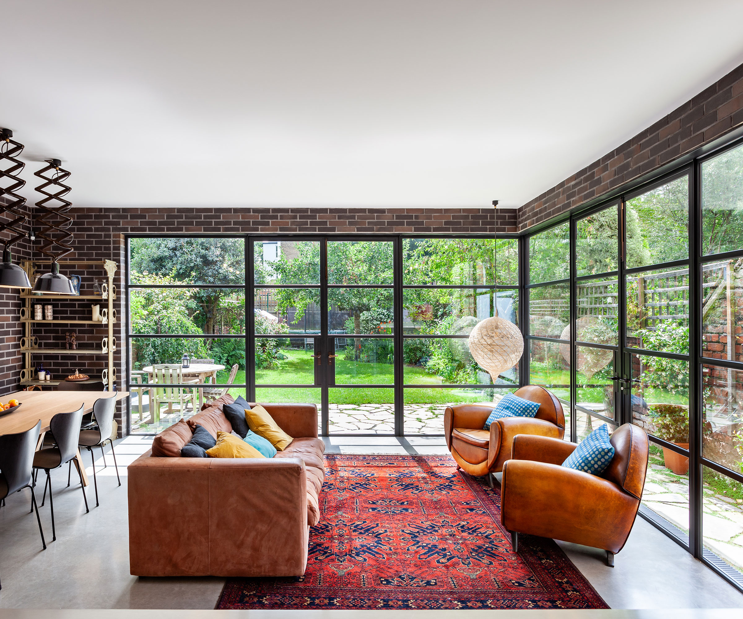 living and dining space with heritage-style glazing on two sides of the room, furnished with a leather sofa, two armchairs and a large patterned rug on the floor