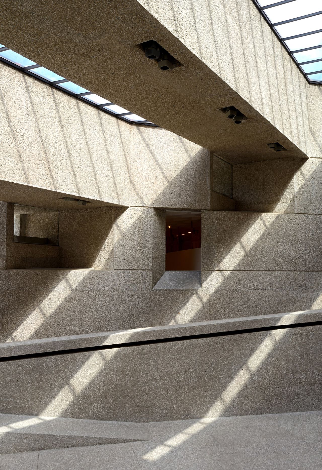 A concrete, brutalist building's zigzagy structure casts lights and shadows all over its surface.