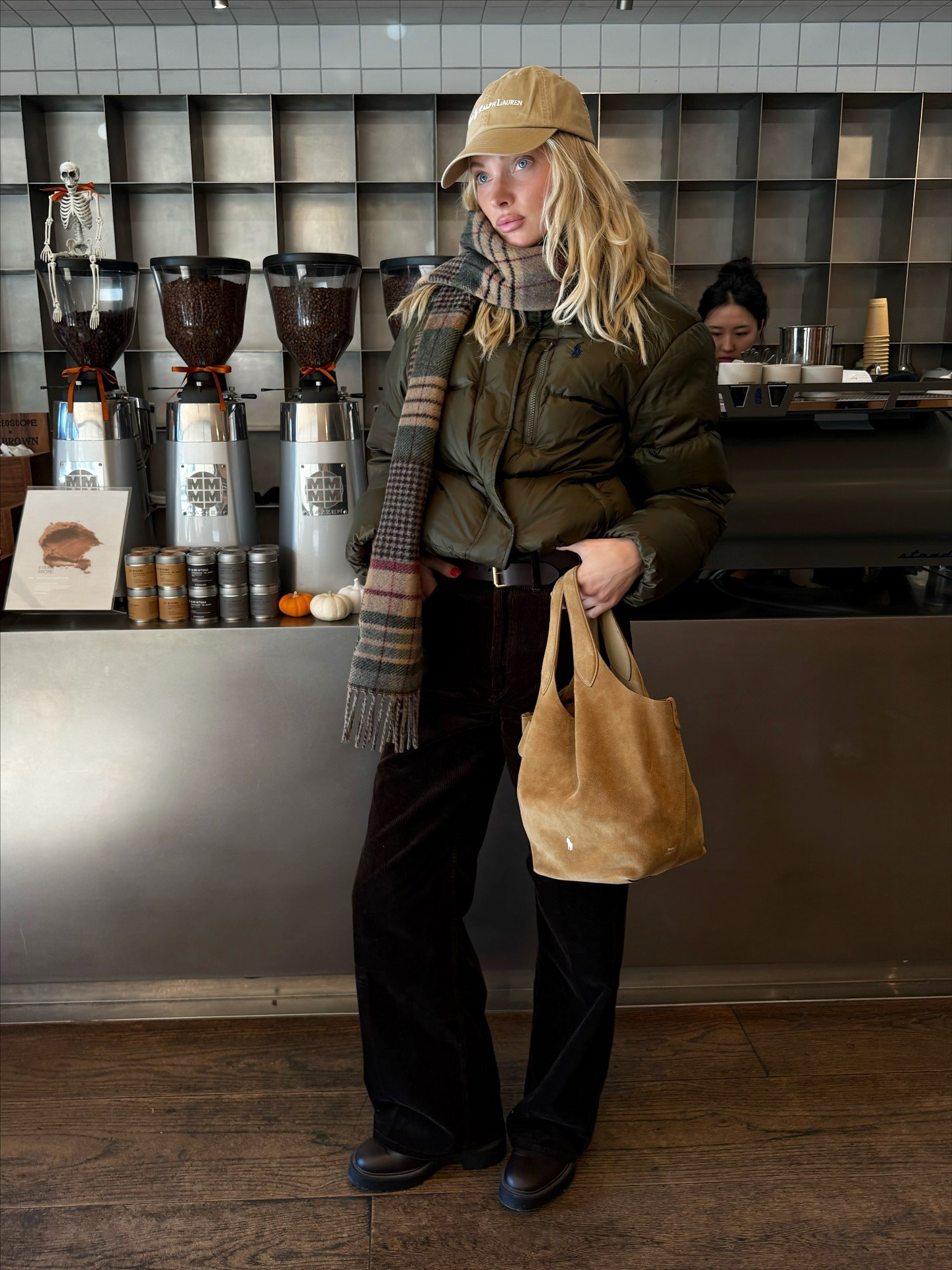 Elsa Hosk wearing a Polo Ralph Lauren baseball cap, olive green puffer jacket, plaid scarf, black pants, and boots